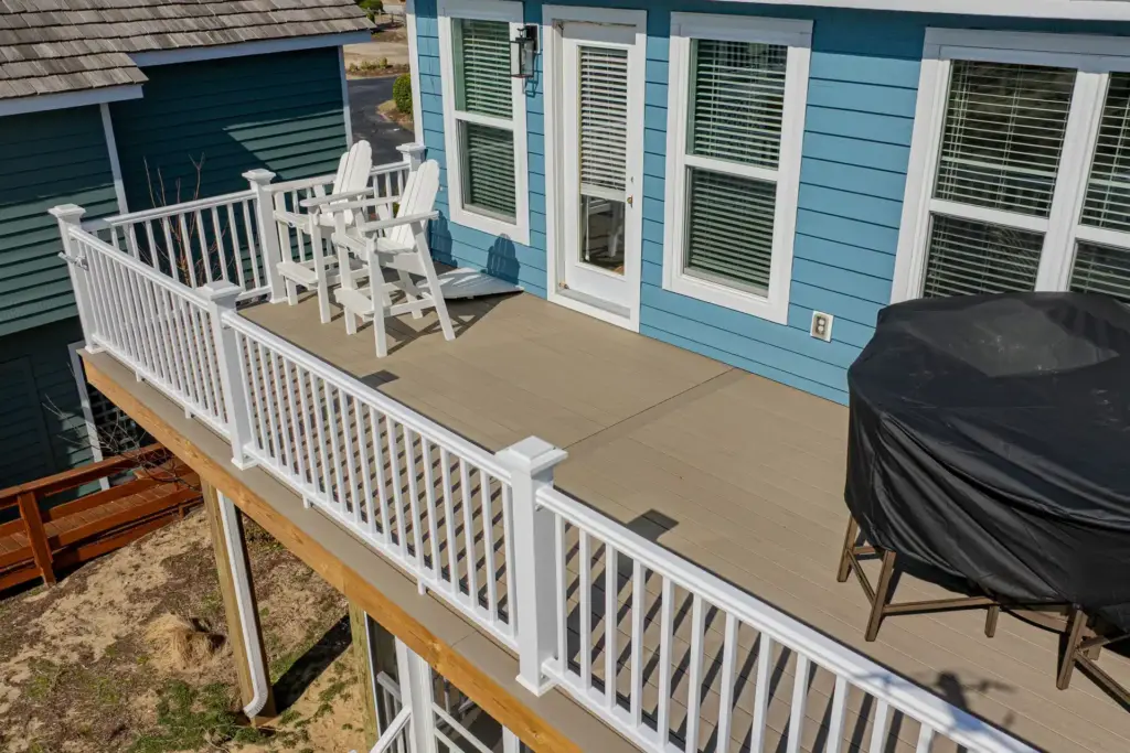aerial-view-of-the-deck-with-two-white-outdoor-chairs-and-covered-furniture-with-white-railing-on-the-blue-house-with-multiple-windows-in-outer-banks-nc