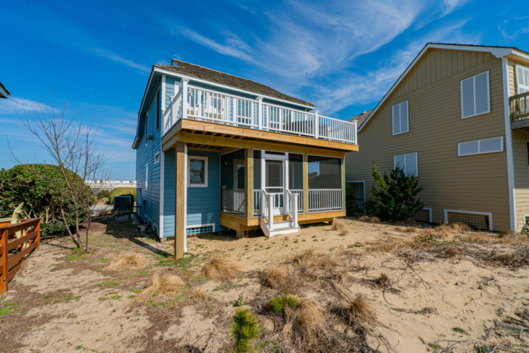 front-screened-in-porch-with-white-railing-and-white-trim-door-and-under-deck-with-outdoor-living-white-chairs-and-covered-furniture-featuring-amazing-sky-view-in-outer-banks-nc