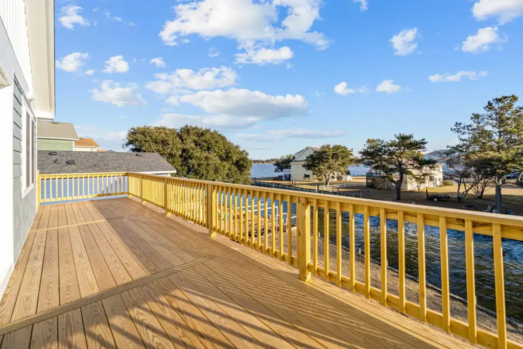 long-wooden-deck-with-railing-on-the-gray-house-featuring-lake-and-blue-sky-with-clouds-view-in-outer-banks-nc