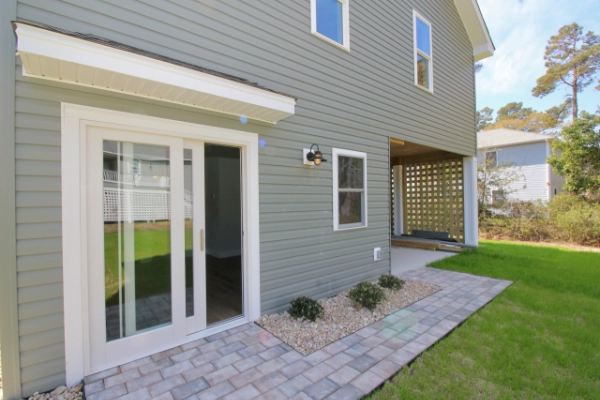 sliding-glass-door-on-the-gray-house-with-patio-and-plants-on-the-ground-with-multiple-windows-featuring-wooden-privacy-screen-on-the-background-in-outer-banks-nc