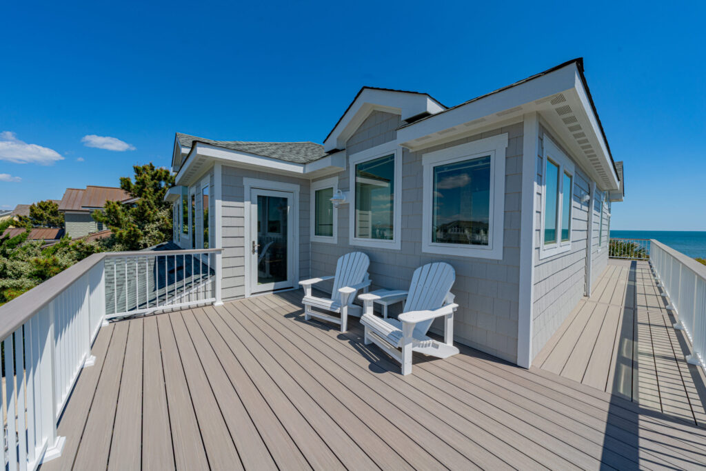 spacious-pvc-deck-on-the-gray-house-with-two-white-chairs-and-multiple-windows-featuring-clear-sky-and-sea-view-in-outer-banks-nc